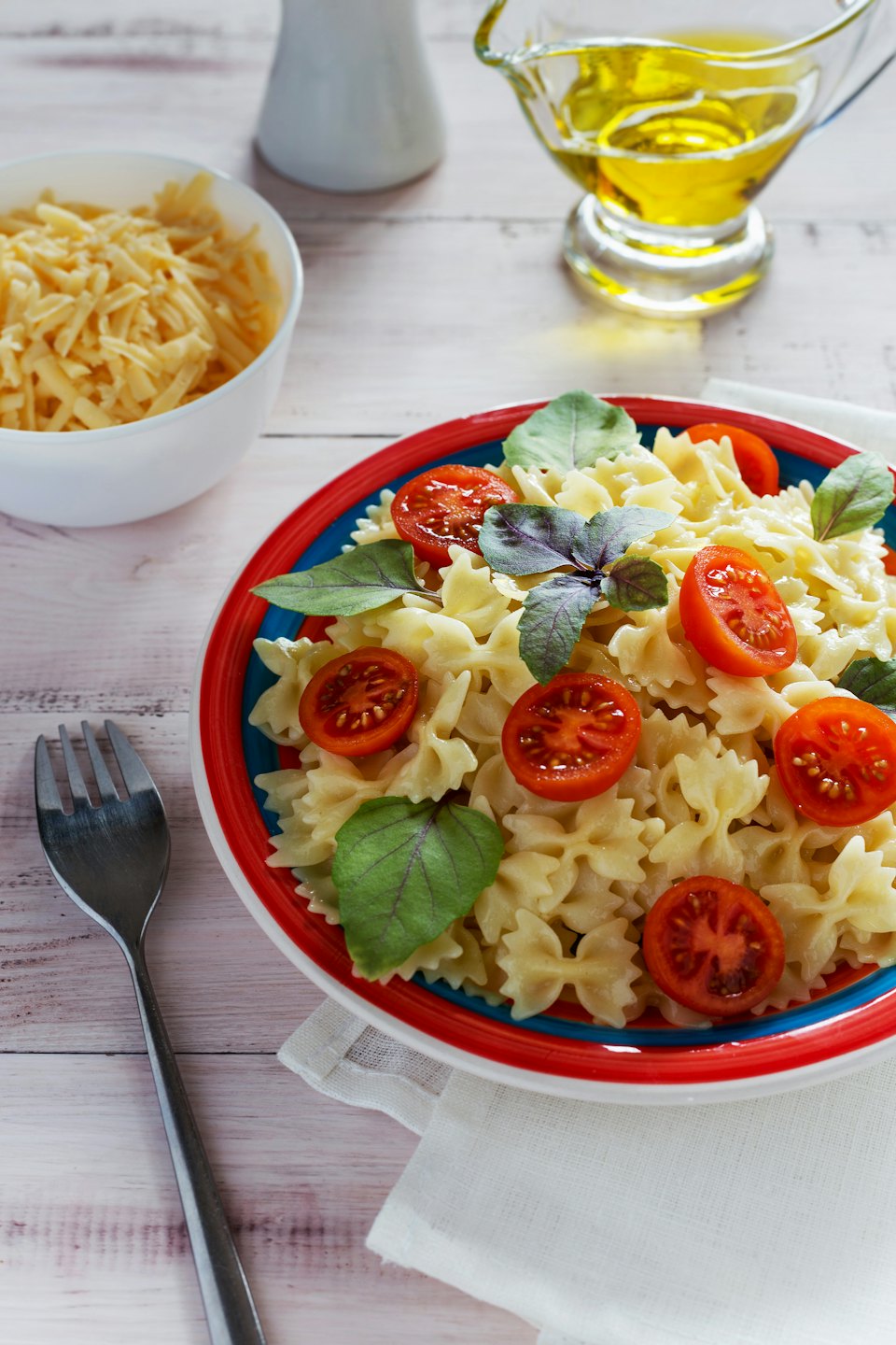 Teller Farfalle-Nudeln mit Kirschtomaten und Basilikum auf einem Tisch.